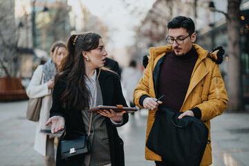 Two business professionals engaged in an animated discussion while walking along a city street,...