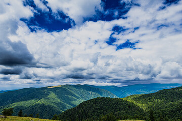 Dense forested mountains stretch beneath a dynamic sky filled with white and dark clouds. Patches...