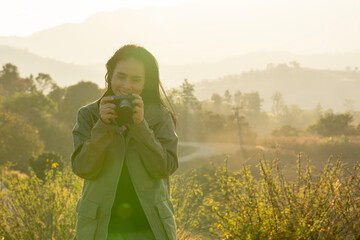 Young Asian female photographer capturing nature in soft evening sunlight, enjoying outdoor...