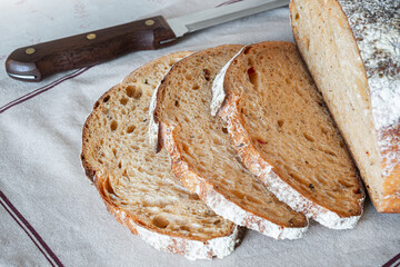 Freshly baked artisanal bread sliced on a linen cloth with a wooden knife displayed artistically in...