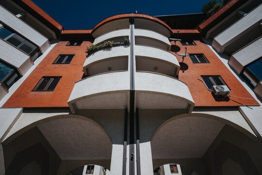 Low angle symmetrical photograph of a modern residential building with a bold and colorful facade design. The architecture features sharp lines and curved balconies under a clear deep blue sky.