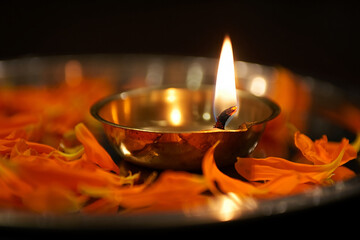 Photo of a lit brass diya with orange petals on a dark background