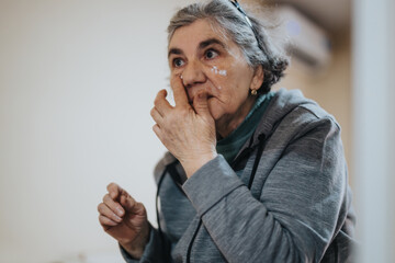 An elderly woman in a gray hoodie touchingly contemplates something while indoors, expressing a...