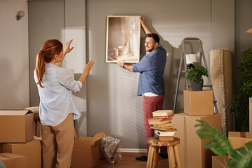 A couple collaborates on decorating their new home. The woman gestures excitedly while the man...