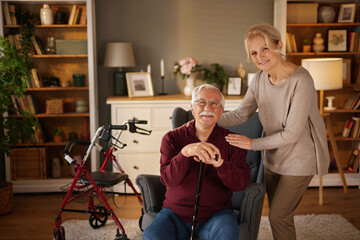 An older gentleman with a cane sits in a chair and smiles as a friendly blonde woman places her...