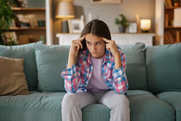 A teenage girl shows frustration while sitting on a couch, reflecting on her concerns and...