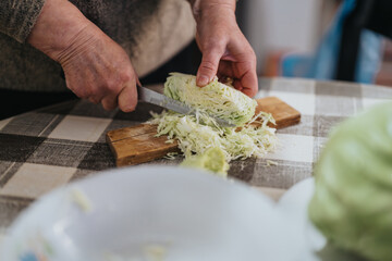 A close-up of hands cutting cabbage with a knife, showcasing a traditional kitchen setting. The image highlights care and precision in preparation, representing culinary skills and homely atmosphere.