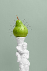 Closeup green pear with safety pins on neoclassical statue against soft green backdrop. Concept of...