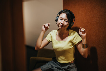 A young woman listens to music through headphones, showing contentment and enjoyment, sitting...