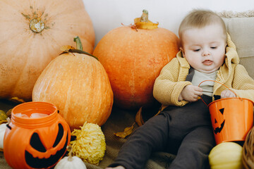 Happy Halloween. Cute happy baby boy sitting with jack o lantern bucket, pumpkins, autumn leaves...
