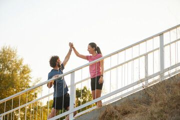 Two individuals share a moment of joy while completing a workout on stairs in a park. Sunlight...