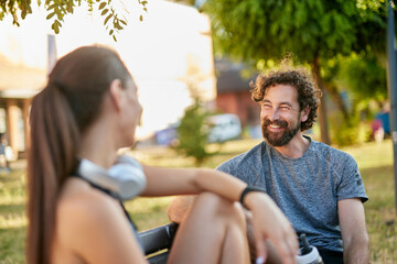 Fototapeta premium Two friends share a moment in a park, discussing their healthy lifestyle after engaging in sports activities. The atmosphere is relaxed and friendly amid lush greenery.