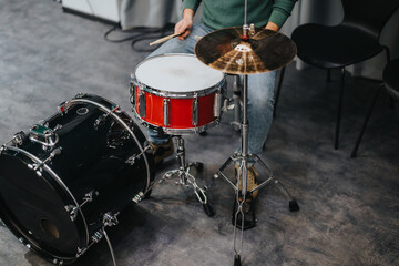 A drummer is practicing on a drum kit in a music studio. The setting is informal, focusing on the...