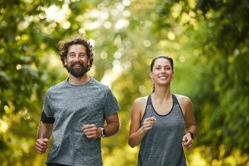 Two individuals are jogging together on a scenic trail surrounded by lush greenery, embracing a...