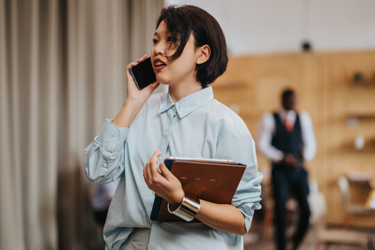A dynamic workplace moment showing a professional woman engaged by managing business tasks via phone and holding a folder, demonstrating productivity in a collaborative co working space.