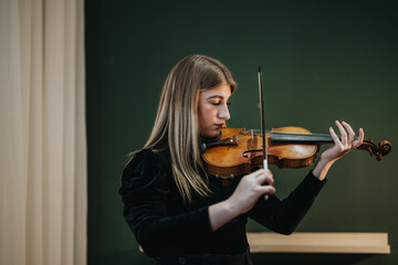 A talented young woman dressed in black plays a violin in a studio, expressing deep emotion and...