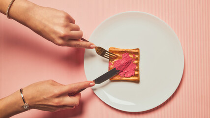 Woman smearing pink lipstick on toast with fork showing amused expression. Concept of mixed beauty and food culture, cosmetic confusion, creative pop art humor.