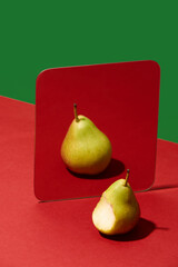 Bitten pear looking into mirror sees full untouched fruit reflection. Concept of idealization,...