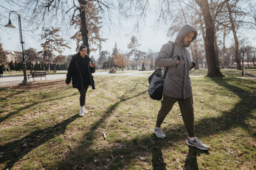 Two teenagers in a park, one with a backpack and the other using a phone, enjoying a sunny day...