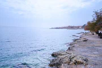 A serene coastal scene with a rocky shoreline and calm sea under a cloudy sky.