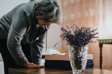 An older woman, wearing casual attire, leans over a table to inspect items beside a decorative...