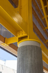 Close-up of a yellow-painted steel beam joined to a concrete column, showcasing industrial...