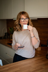 A woman standing in her kitchen and drinking her morning coffee