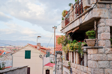 A charming stone house with a balcony adorned with plants, set in a quaint European village. The...