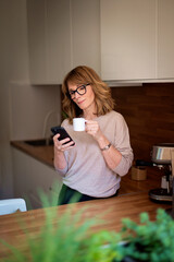 A woman standing in her kitchen and drinking her morning coffee