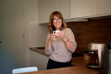 A woman standing in her kitchen and drinking her morning coffee