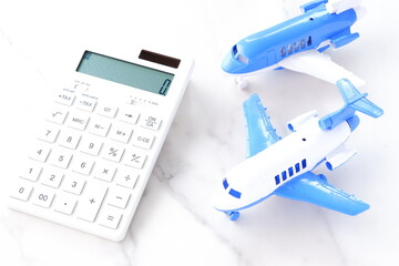 電卓と飛行機で、高騰する航空券代と、高騰する旅行代金のイメージ
