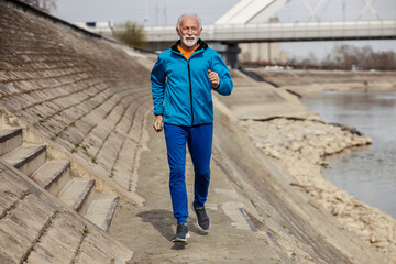 Front view of senior sportsman running towards camera on riverbank.
