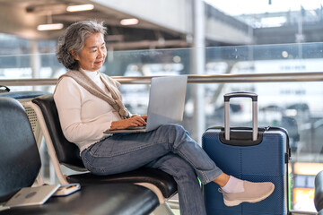 Senior woman working on laptop at airport terminal enjoying online connection, travel lifestyle and...