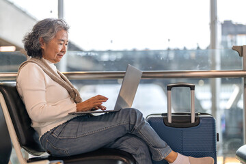 Senior woman working on laptop at airport terminal enjoying online connection, travel lifestyle and...