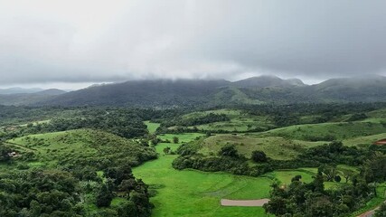 Cinematic drone view of lush mountains, farmlands, a valley, curvy road, and misty winter clouds
