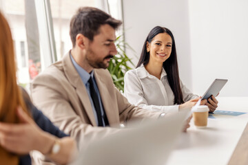 Selective focus on female executive sitting at conference table with her colleagues and using tablet while smiling at camera.