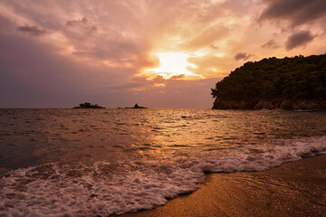 Vivid sunset over a serene beach, featuring soft waves, a colorful sky, and silhouetted landscapes.