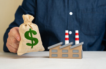 Man holding dollar moneybag near factory. Purchase of industrial assets and production. Investments...