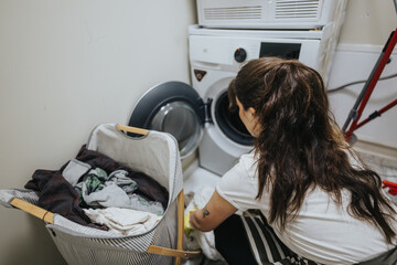A woman organizes laundry by placing clothes into a washing machine in a clean and organized...