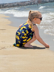 Little girl in a patterned summer dress enjoys a sunny day at the beach. The dress features a...