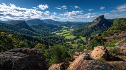 Obraz premium A panoramic view of a lush green valley surrounded by rocky mountains under a partly cloudy blue sky.