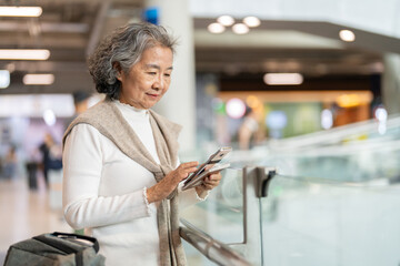 Senior asian woman holding passport and smartphone at airport showing digital travel, trip...