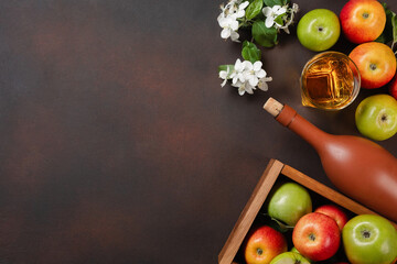 Ripe red and green apples in wooden box with branch of white flowers, glass and bottle of cider on...