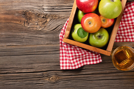 Ripe red and green apples in wooden box with glass of fresh juice on a wooden table