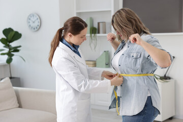 Weight loss. Nutritionist measuring overweight woman's waist with tape in clinic