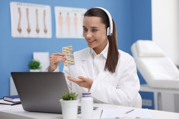 Doctor in headphones with pills having online consultation via laptop indoors