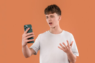Teenager expressing frustration while looking at a smartphone against an orange background in a...