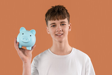 Young boy holds blue piggy bank and smiles against an orange background while promoting saving...