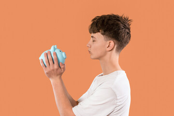 Young person contemplating savings while holding a blue piggy bank in front of an orange background