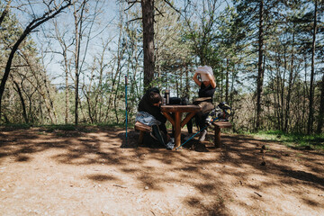 Obraz premium Two hikers taking a break at a picnic spot in a tranquil forest setting, showcasing outdoor adventure and nature's beauty.